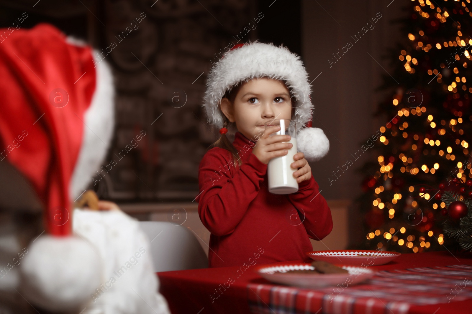 Photo of Cute little child with glass of milk at table in dining room. Christmas time