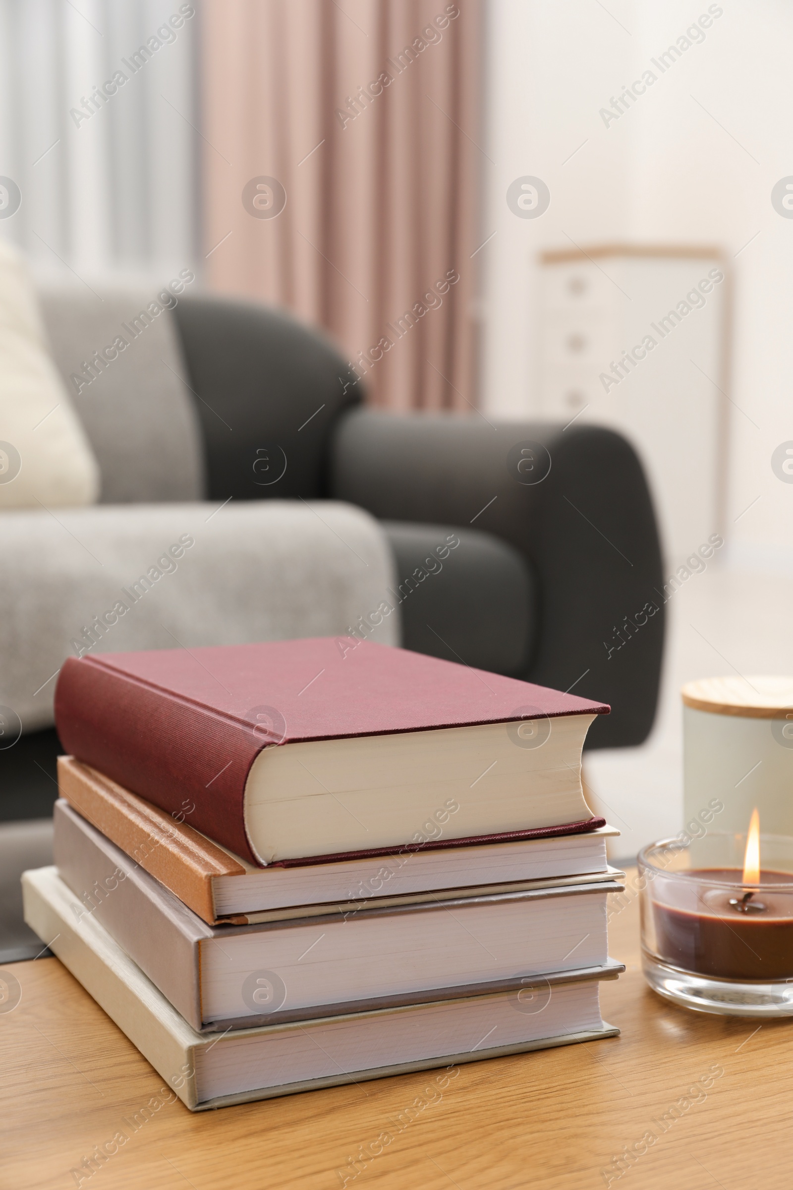 Photo of Books and burning candle on wooden table indoors, space for text