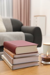 Books and burning candle on wooden table indoors, space for text