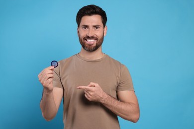Happy man holding condom on light blue background. Safe sex
