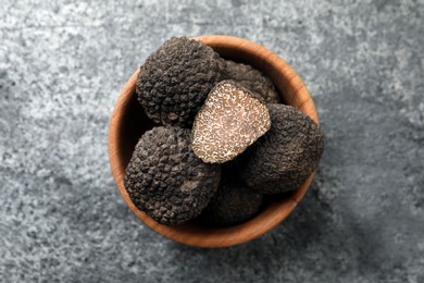 Photo of Black truffles in wooden bowl on grey table, top view