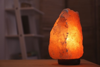 Photo of Himalayan salt lamp on table in dark room. Blurred background with space for text