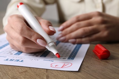 School grade. Teacher writing letter A with plus symbol on answer sheet at wooden table, closeup