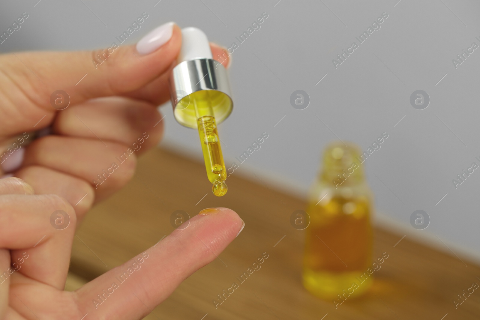 Photo of Young woman dripping essential oil on finger against blurred background, closeup