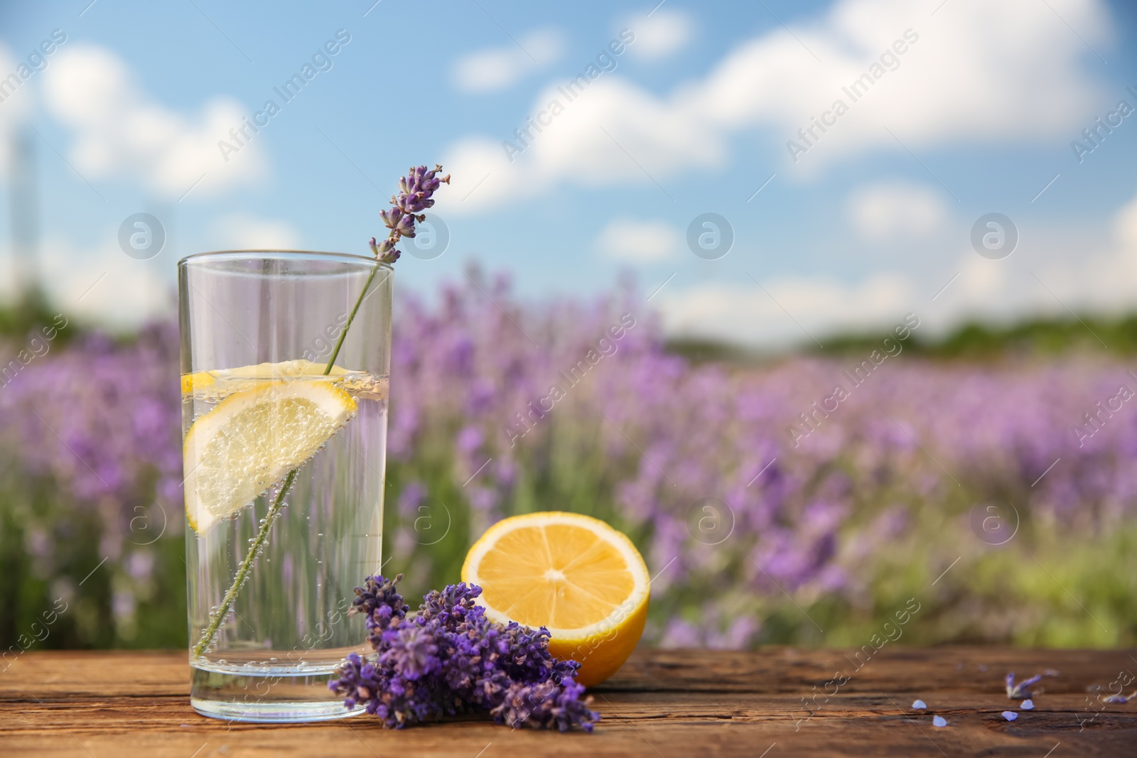 Photo of Lemonade with lemon slices and lavender flowers on wooden table outdoors, closeup. Space for text