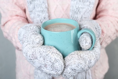 Photo of Woman with knitted mittens holding cup of delicious cocoa drink, closeup