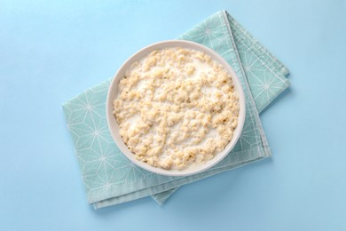 Photo of Tasty boiled oatmeal in bowl on light blue table, top view