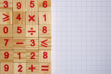 Wooden cubes with mathematical symbols and numbers on sheet of grid paper, flat lay. Space for text