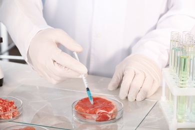 Scientist injecting liquid into meat sample in laboratory, closeup