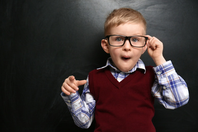 Photo of Cute little child wearing glasses near chalkboard. First time at school