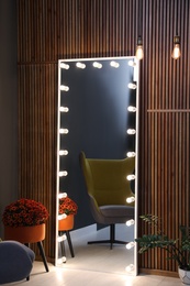 Full length dressing mirror with lamps and armchair in stylish room interior