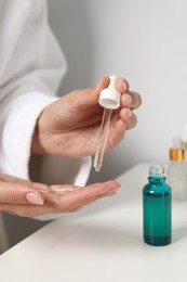 Woman applying cosmetic serum onto her finger at white table, closeup