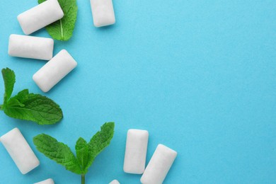 Photo of Tasty white chewing gums and mint leaves on light green background, flat lay. Space for text