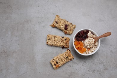 Photo of Tasty granola bars and ingredients on grey table, flat lay. Space for text