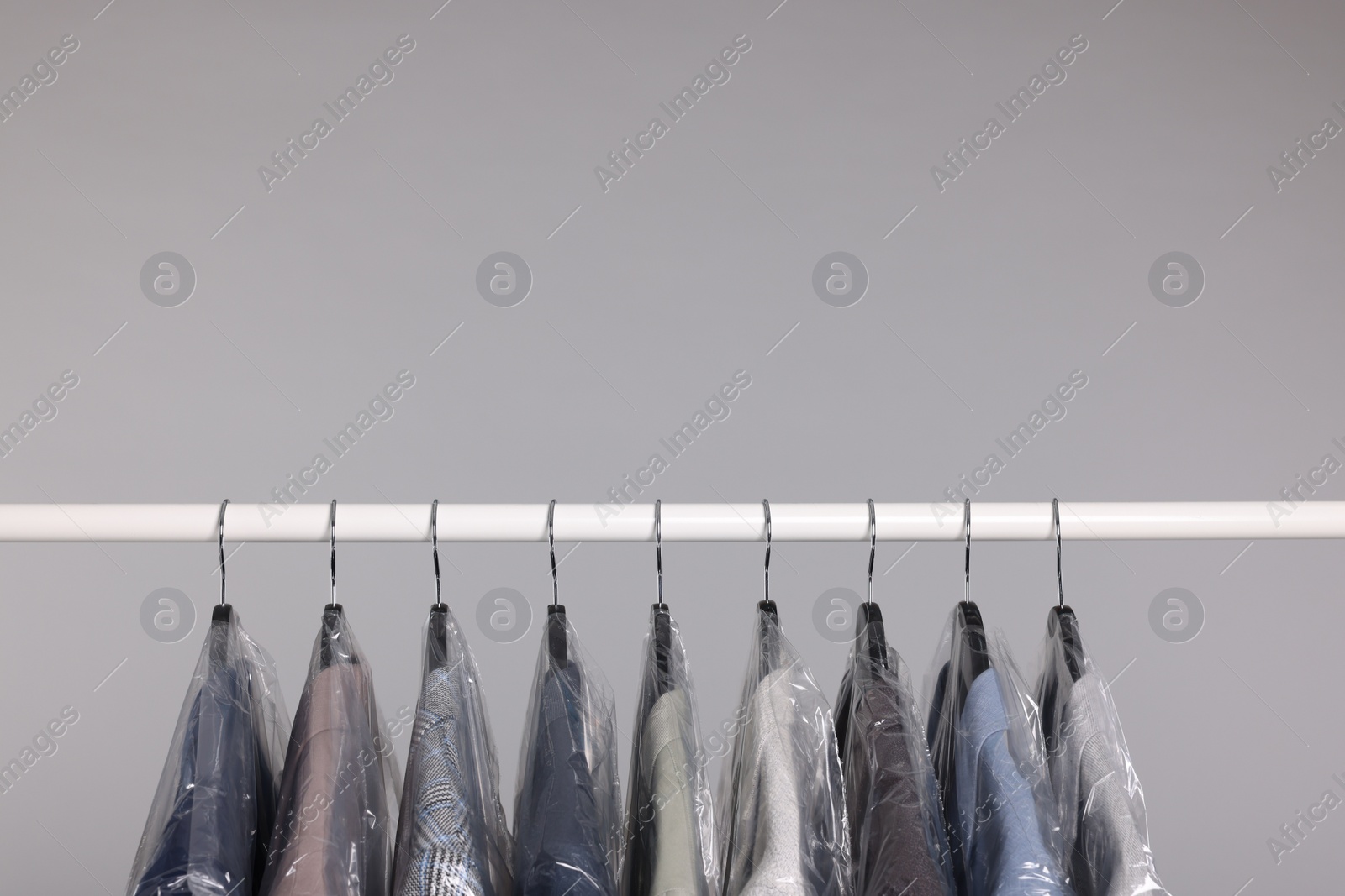 Photo of Dry-cleaning service. Many different clothes in plastic bags hanging on rack against grey background, space for text