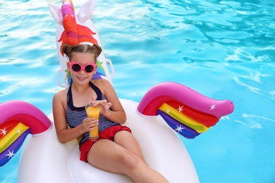Happy girl with drink on inflatable unicorn in swimming pool