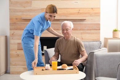 Photo of Nurse serving breakfast to elderly man indoors. Assisting senior people