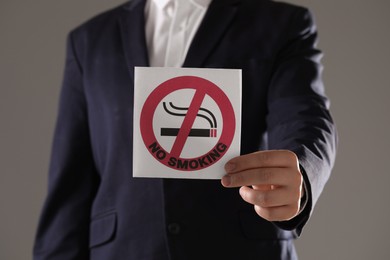 Man holding card with no smoking sign on gray background, closeup