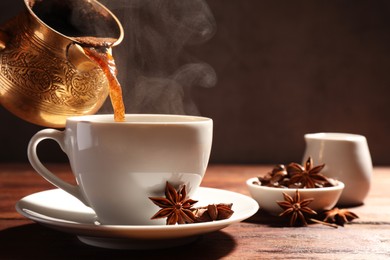 Photo of Pouring aromatic hot coffee into cup and anise stars on wooden table. Space for text