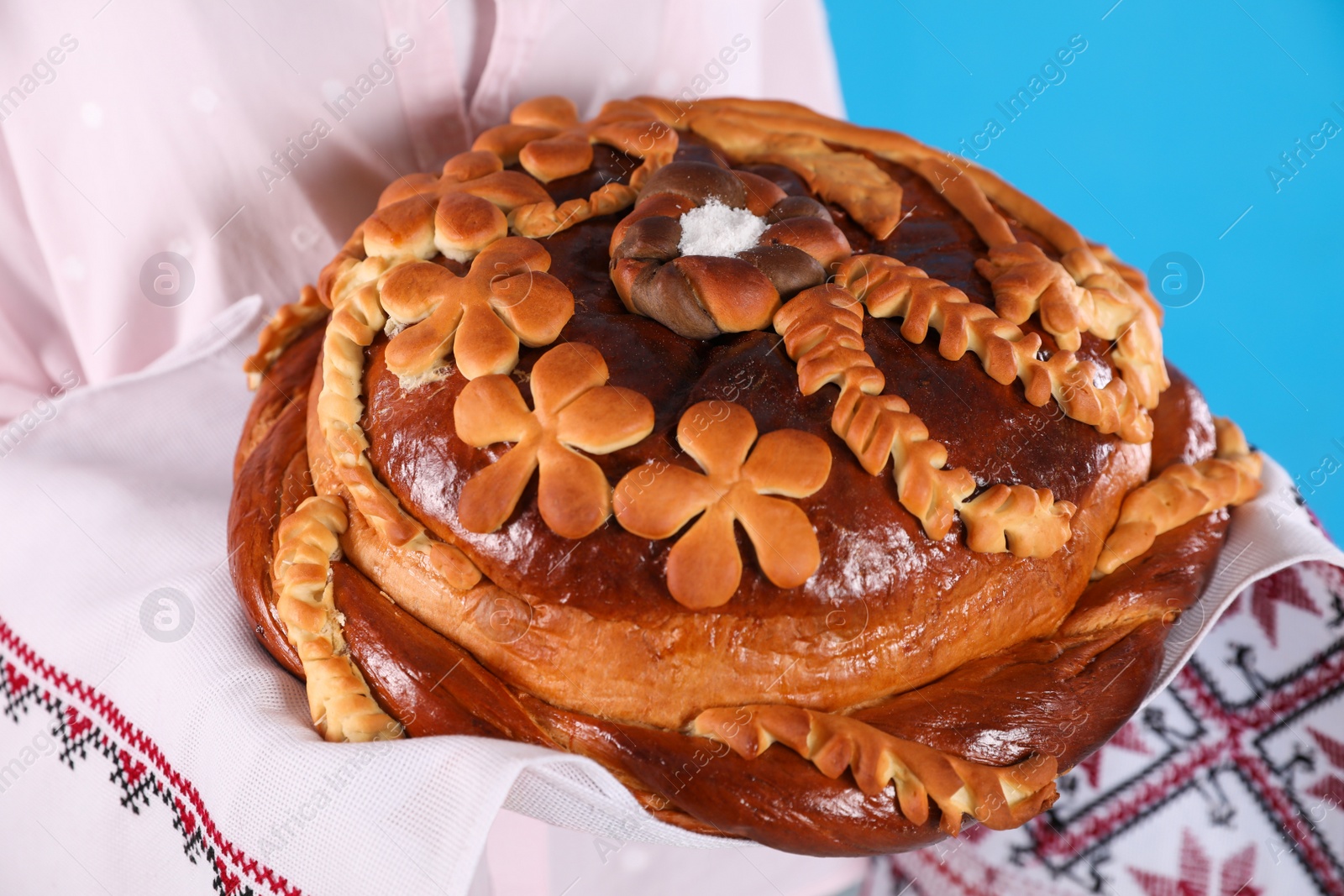 Photo of Woman with korovai on light blue background, closeup. Ukrainian bread and salt welcoming tradition