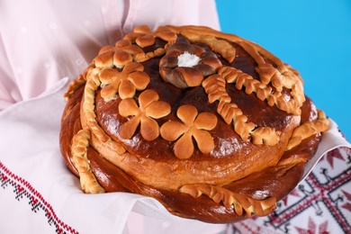 Photo of Woman with korovai on light blue background, closeup. Ukrainian bread and salt welcoming tradition