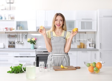 Photo of Young woman preparing lemonade on table in kitchen. Natural detox drink