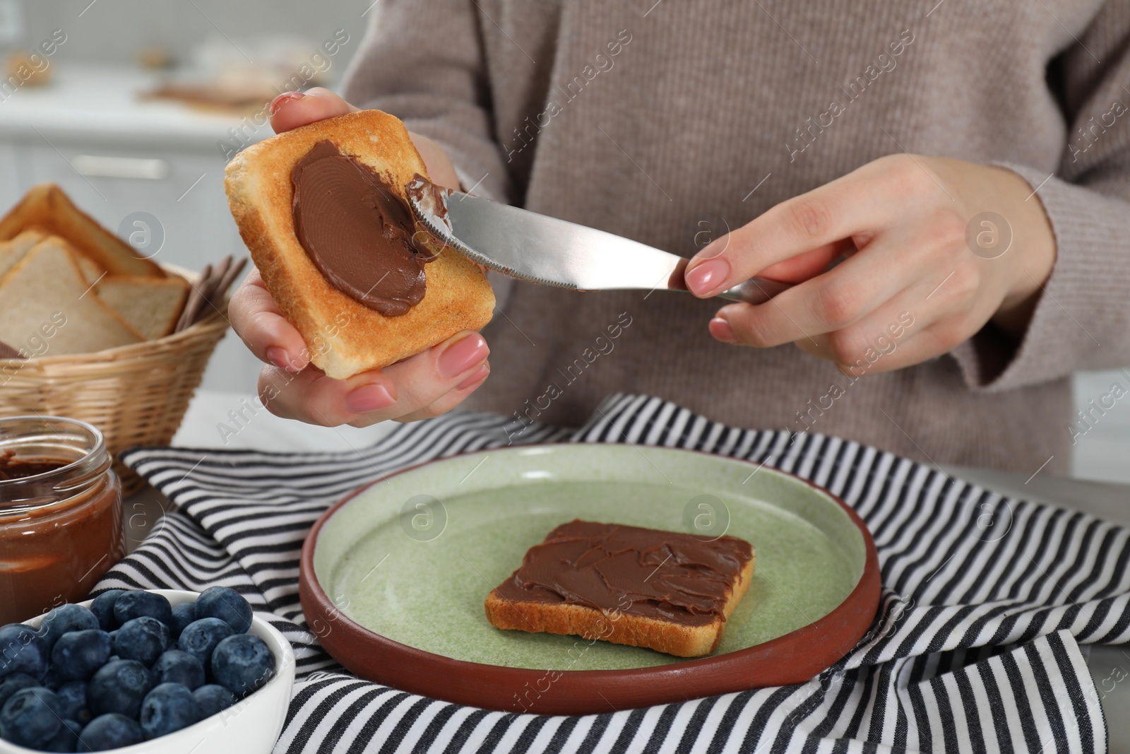 Photo of Woman spreading tasty nut butter onto toast at table, closeup