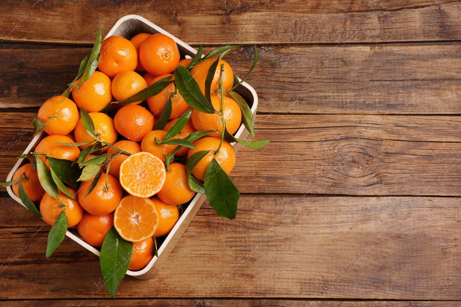 Photo of Fresh tangerines with green leaves in crate on wooden table, top view. Space for text