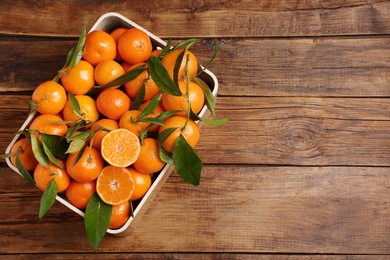 Fresh tangerines with green leaves in crate on wooden table, top view. Space for text