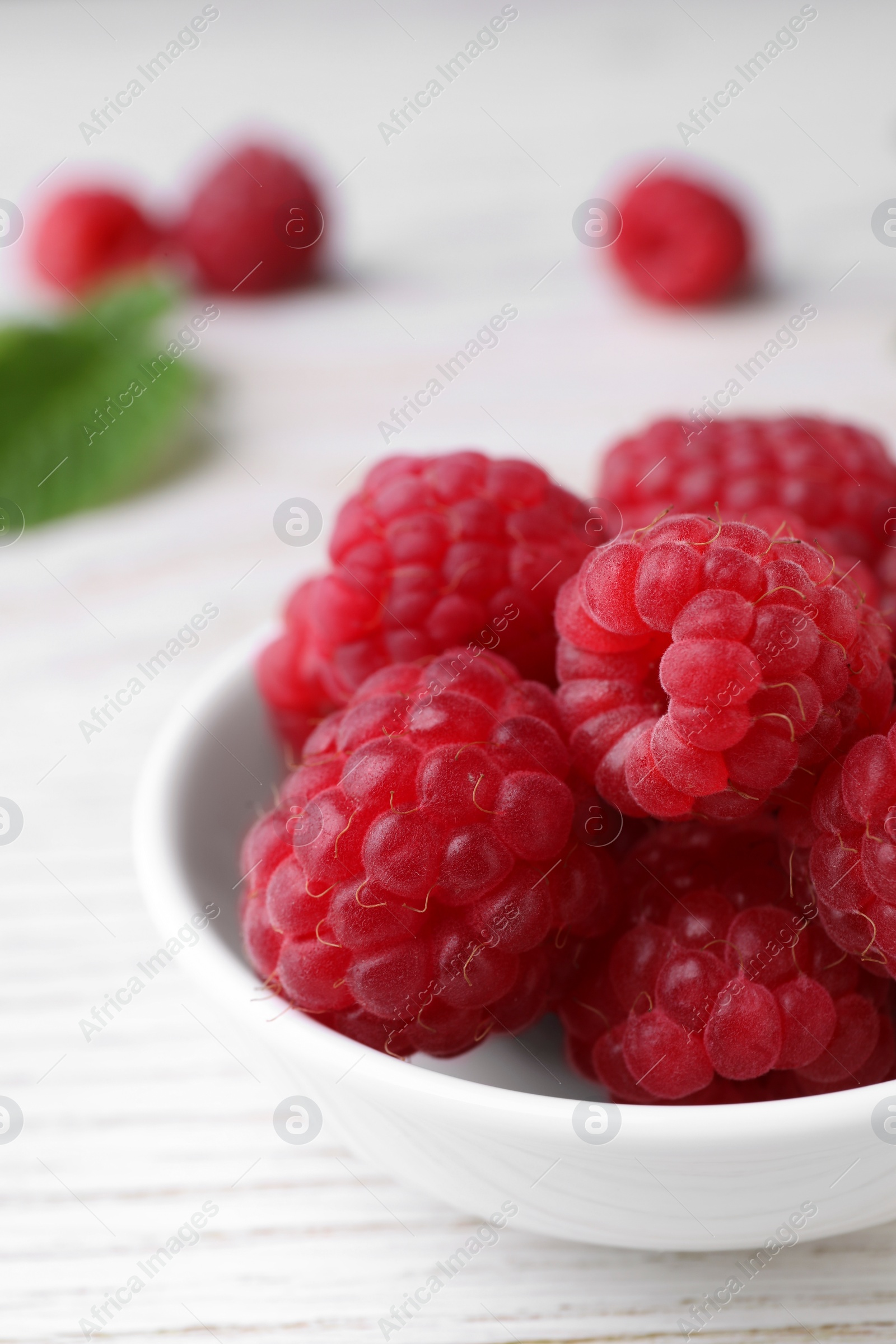 Photo of Tasty ripe raspberries in bowl on white wooden table, closeup. Space for text