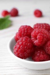 Tasty ripe raspberries in bowl on white wooden table, closeup. Space for text
