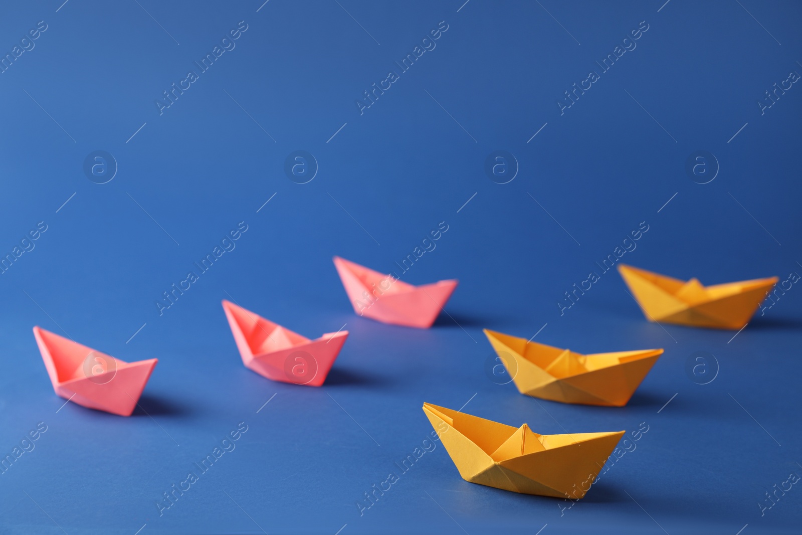 Photo of Many pink and orange handmade paper boats on blue background. Origami art