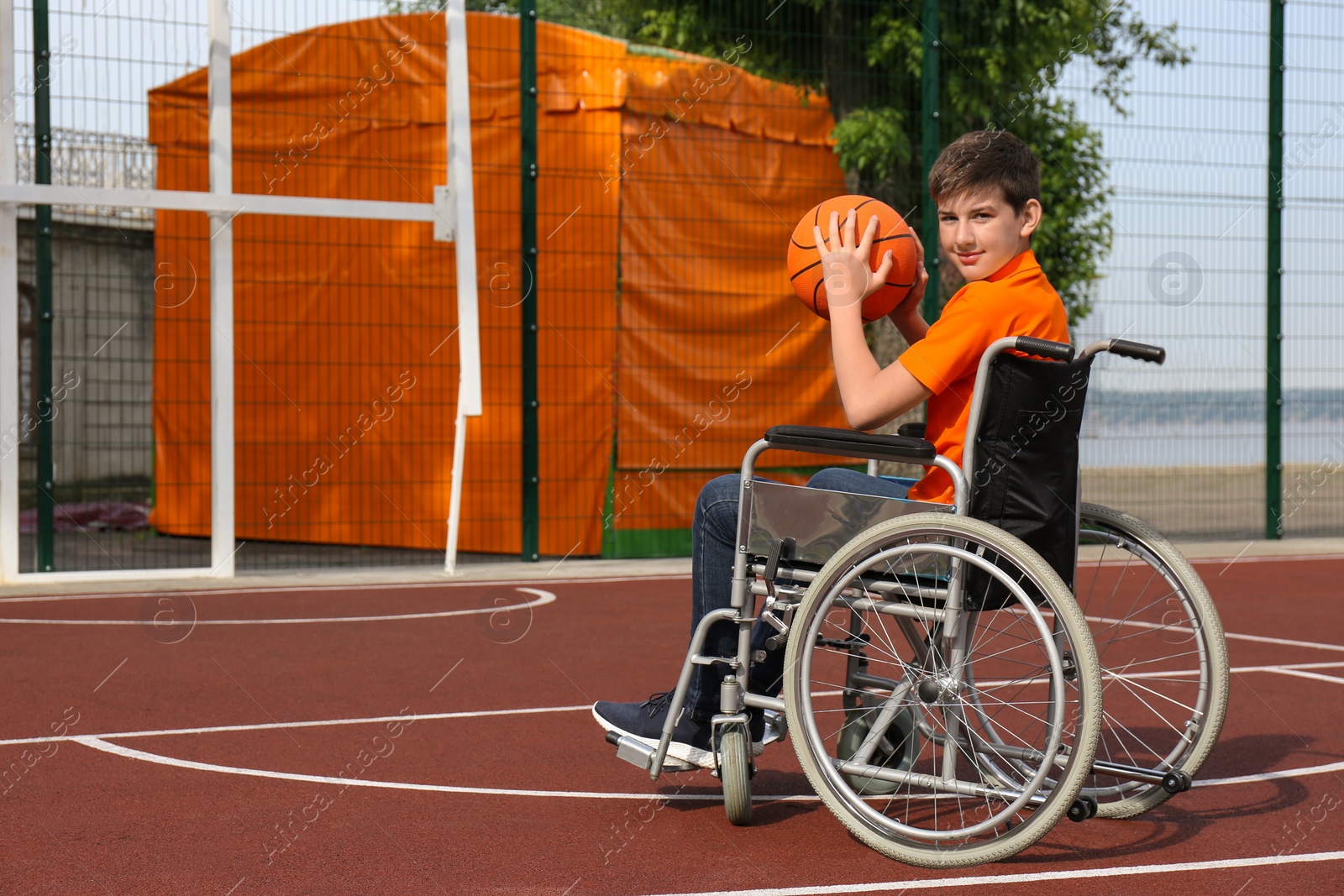 Photo of Disabled teenage boy in wheelchair with basketball ball at outdoor court