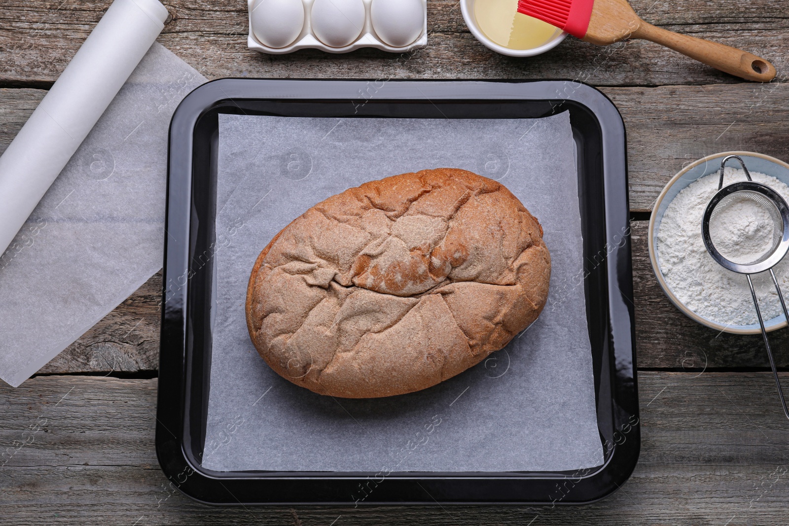 Photo of Parchment paper, baking pan with tasty homemade bread and different ingredients on wooden table, flat lay