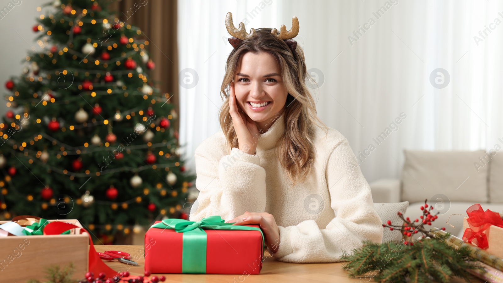 Photo of Young woman with beautifully wrapped Christmas gift at home