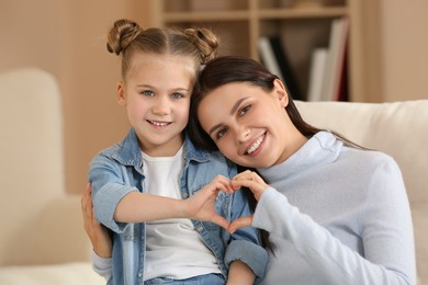 Little girl and her mother making heart with hands at home