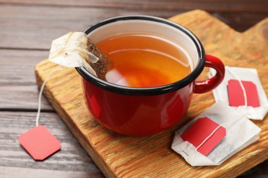 Tea bags and cup of hot beverage on wooden table, closeup