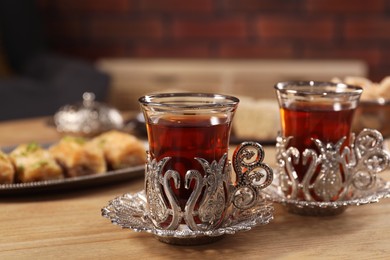 Photo of Glasses of traditional Turkish tea in vintage holders on wooden table