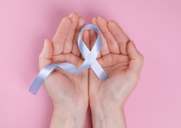 International Psoriasis Day. Woman with light blue ribbon as symbol of support on pink background, top view