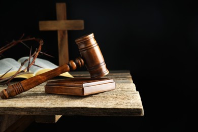 Photo of Judge gavel, bible, cross and crown of thorns on wooden table against black background. Space for text