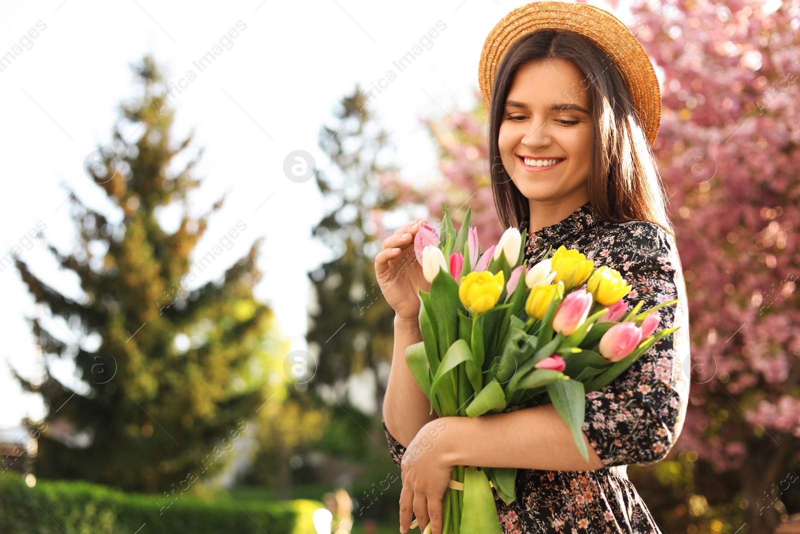 Photo of Beautiful young woman with bouquet of tulips in park on sunny day, space for text