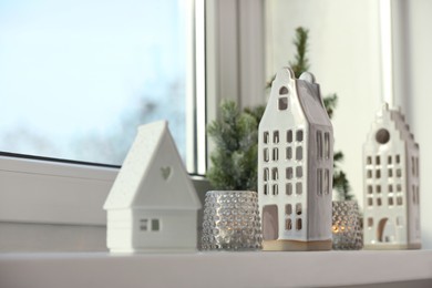 Photo of Beautiful house shaped candle holders and small fir trees on windowsill indoors, space for text