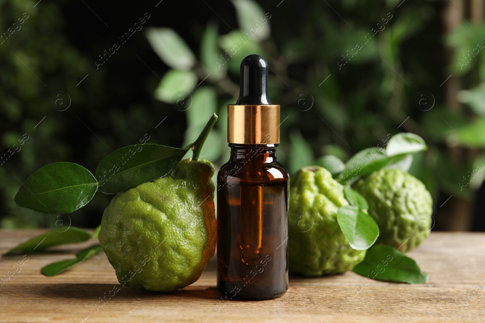 Photo of Glass bottle of bergamot essential oil and fresh fruits on wooden table