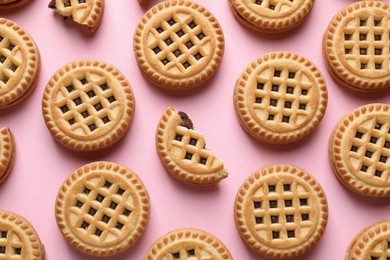 Tasty sandwich cookies with cream on pink background, flat lay