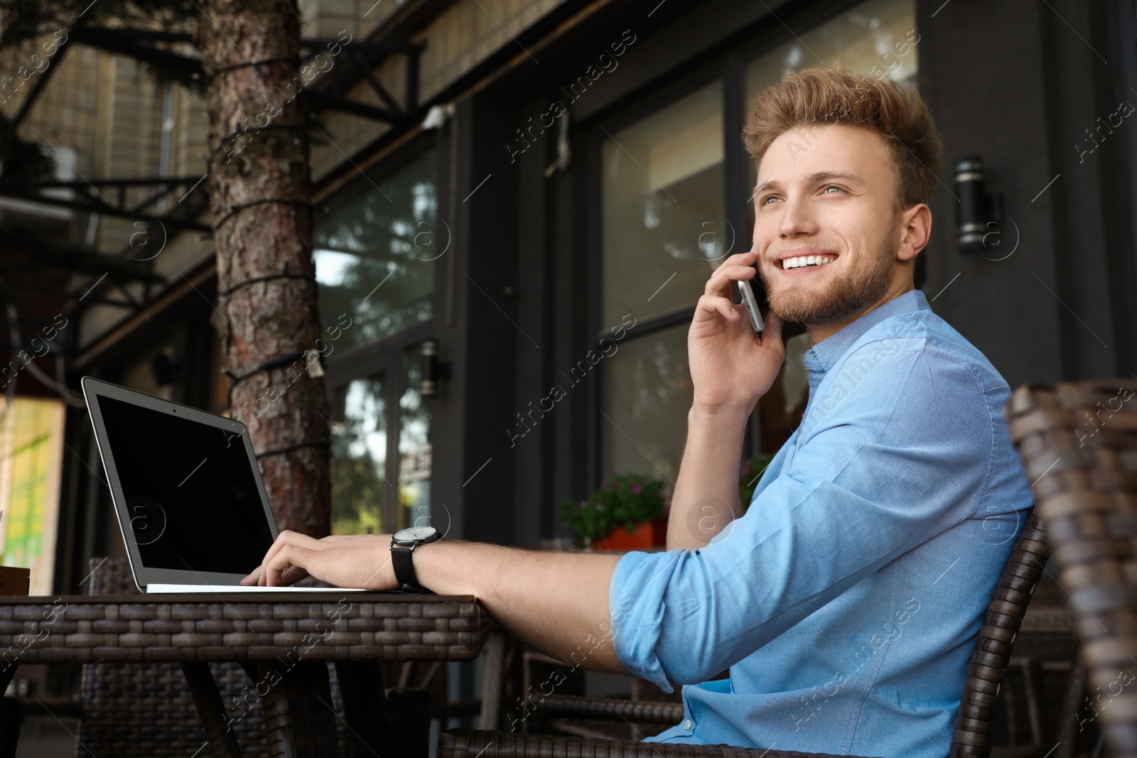 Photo of Handsome young man with laptop sitting at table in cafe outdoors