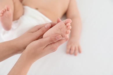 Photo of Mother and her cute child on white bed, closeup. Baby massage and exercises
