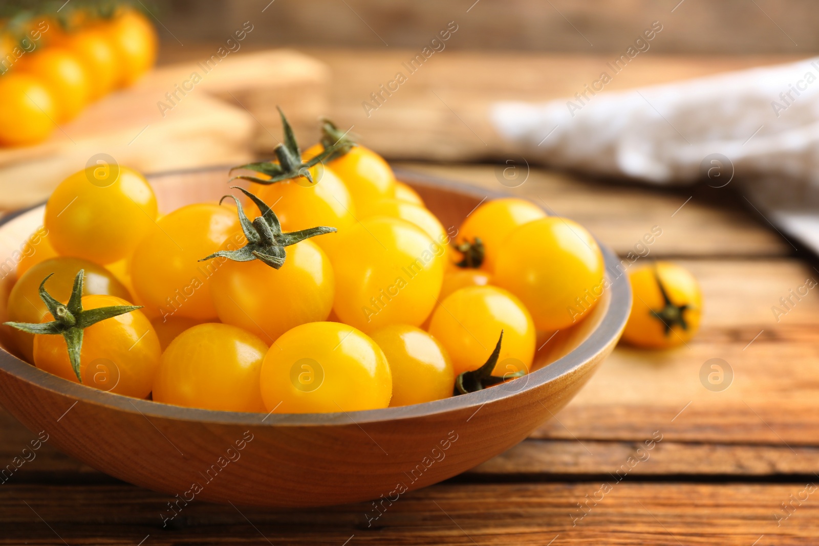 Photo of Ripe yellow tomatoes in bowl on wooden table, closeup