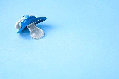 One baby pacifier on light blue background. Space for text