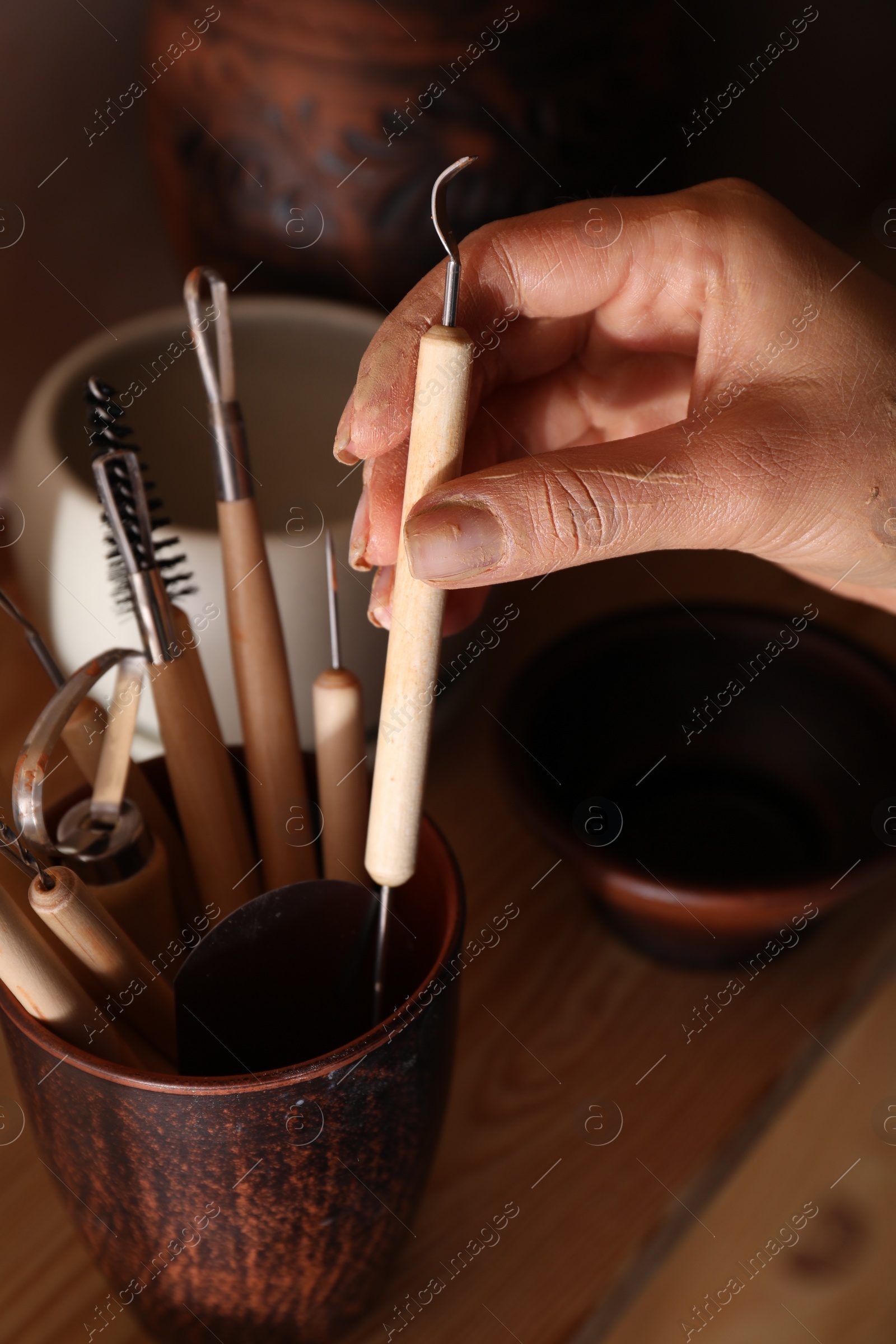 Photo of Woman taking clay crafting tool from cup in workshop, closeup