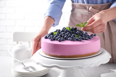 Photo of Young woman decorating tasty blueberry cake with mint at table, closeup